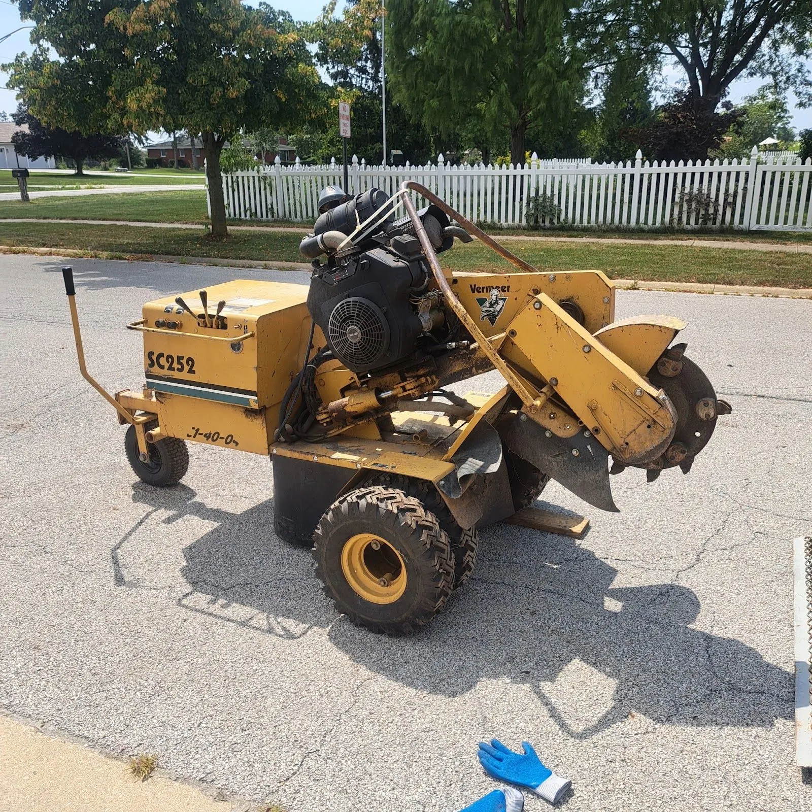 A yellow Vermeer stump grinder parked on a residential street, ready to unload for a job